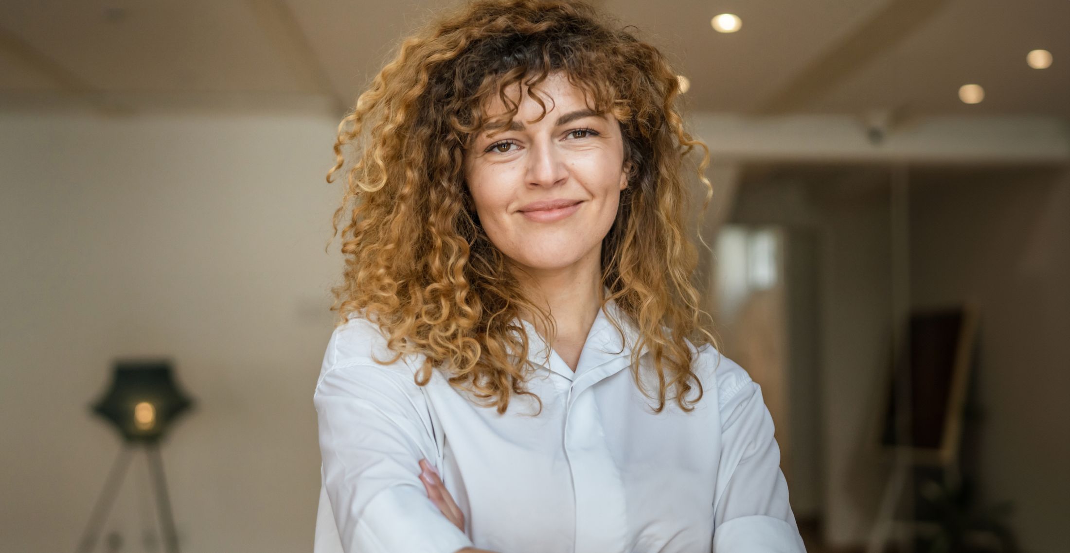 Smiling woman with curly hair in bright setting.
