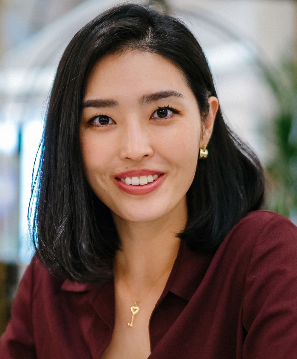Smiling woman in a maroon shirt, key necklace.