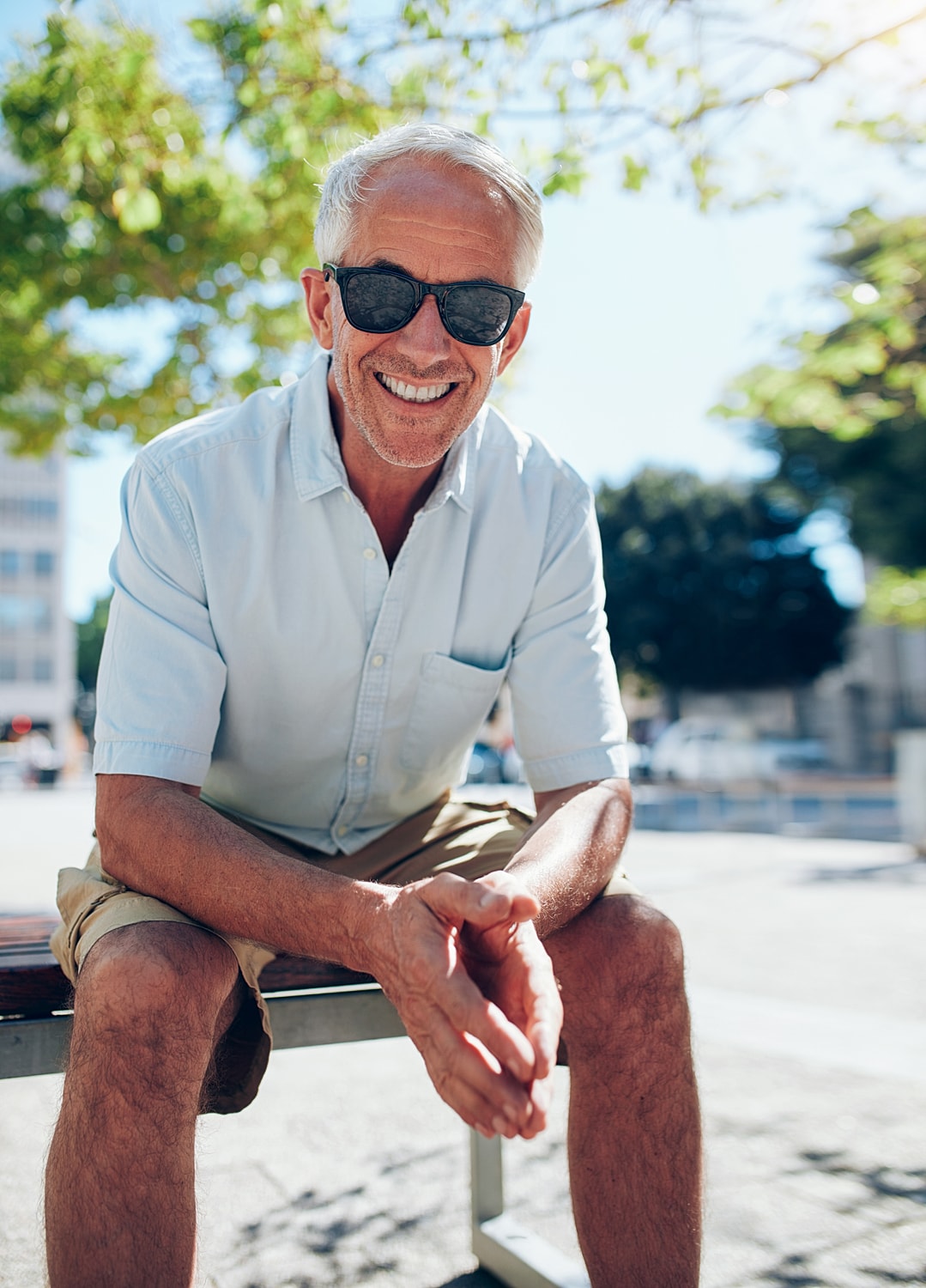 Smiling older man sitting outdoors in sunglasses.