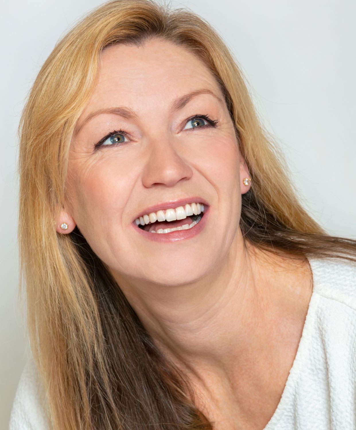 Smiling woman with long blonde hair and earrings.