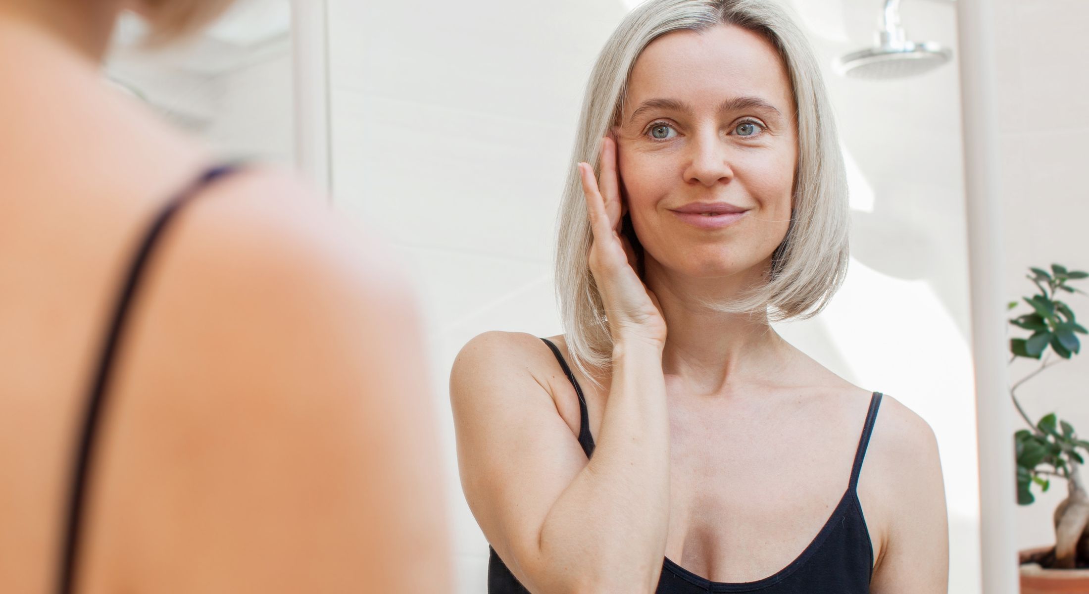 Woman touching her face in bathroom mirror.