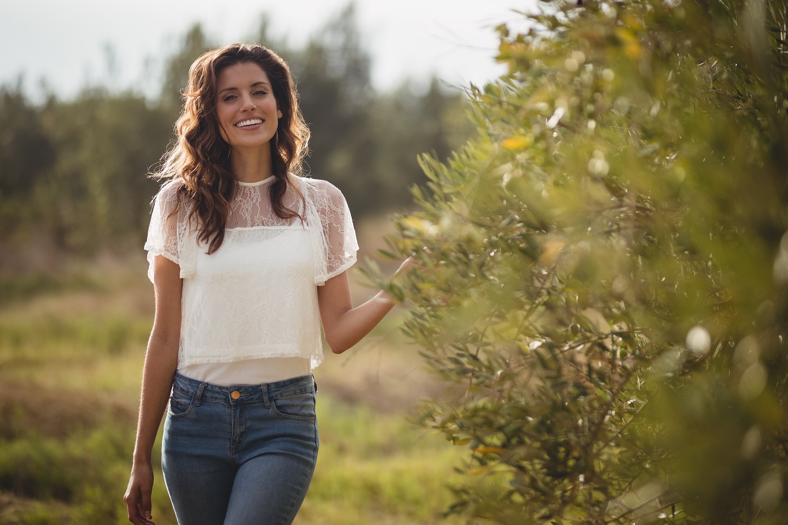 Woman smiling in nature, wearing a white top.
