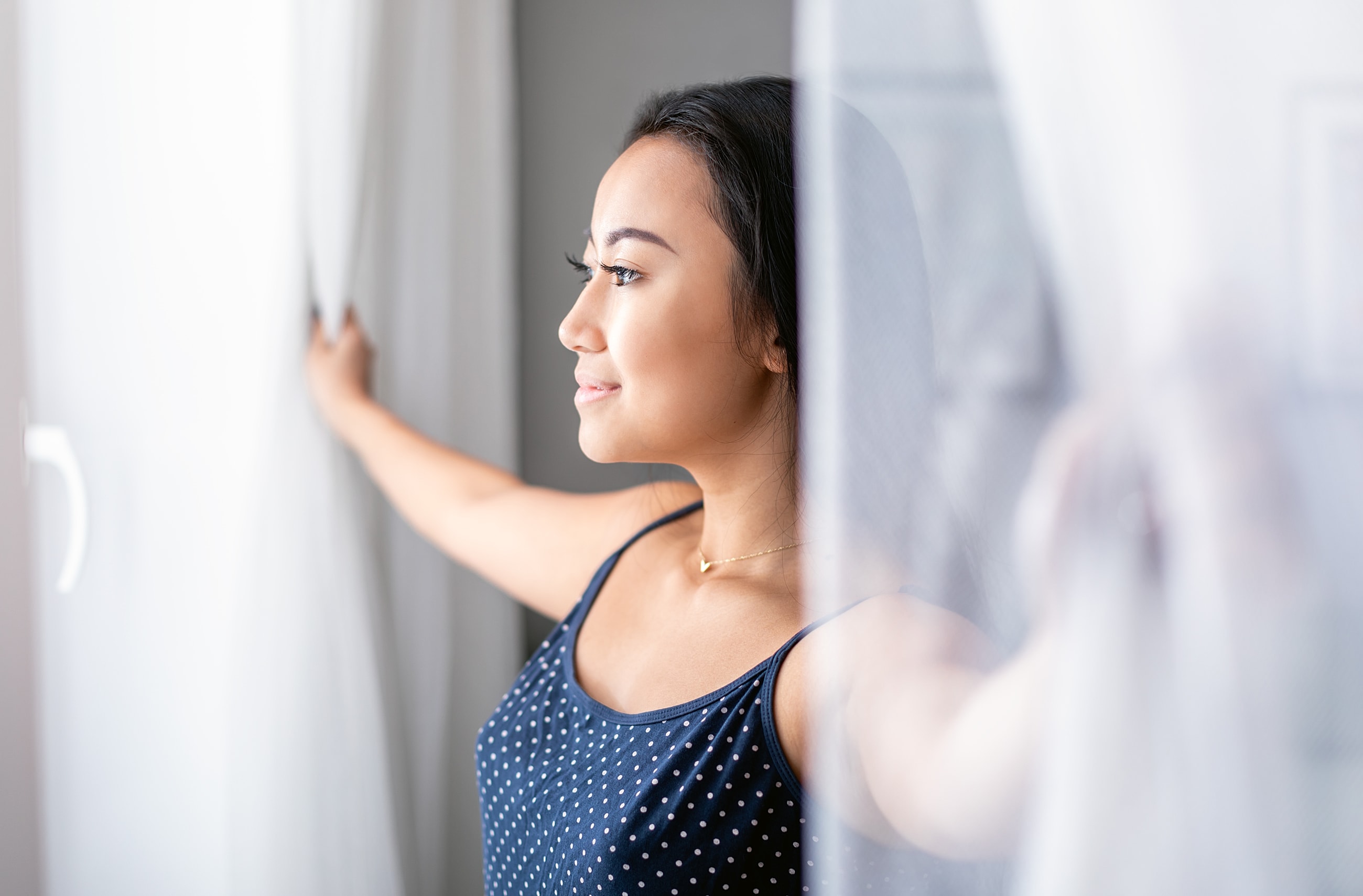 Woman pulling back curtains in bright room.