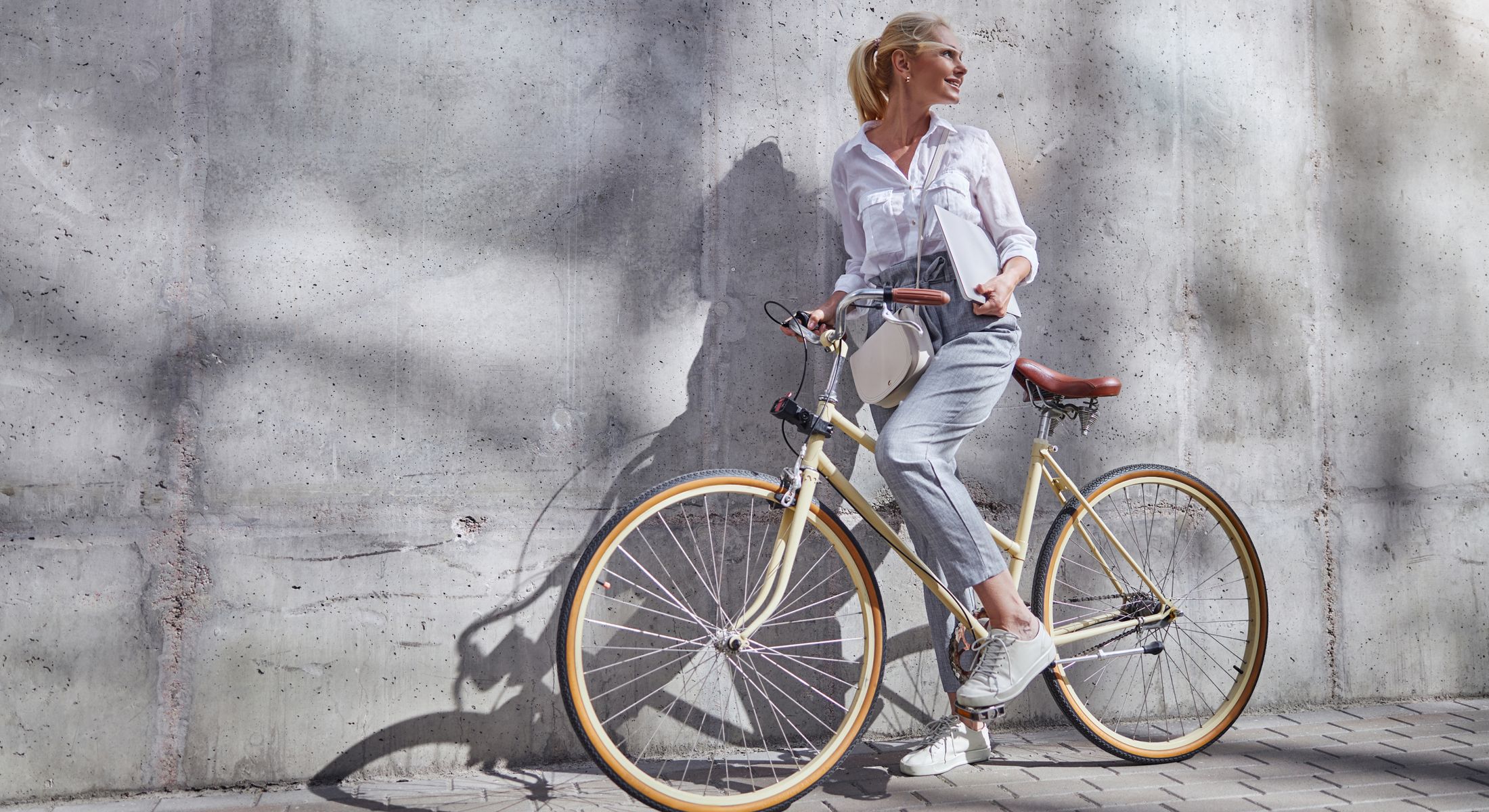 Woman leaning against bike near concrete wall.